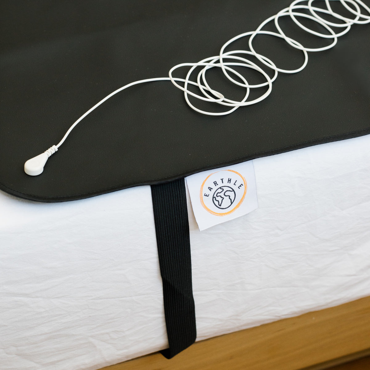Erdungskabel aufgerollt auf der schwarzen Schlafmatte auf einem gemachten Bett