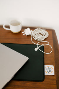 Erdungsstecker und aufgerolltes Kabel auf einem Schreibtisch neben der Schreibtischmatte und einem Laptop