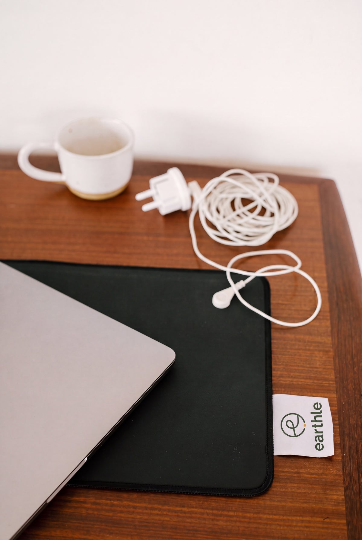 Earthle Erdungs-Schreibtischmatte auf einem Holzschreibtisch mit Laptop, Kaffeetasse und dem aufgerollten Erdungskabel